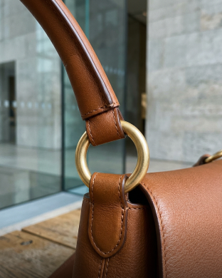 Gold ring joint attaching a handle to a brown leather bag