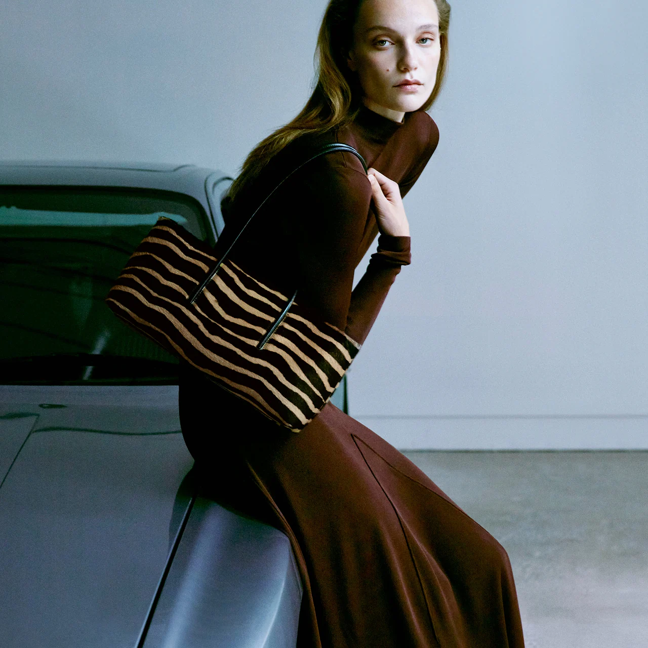 Woman carrying a striped Pakito shoulder bag beside a car