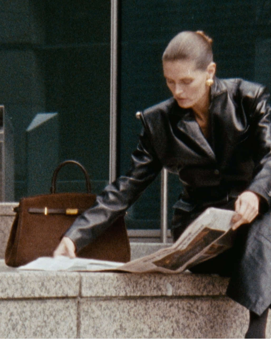 Woman leaning over a brown handbag on an outdoor table