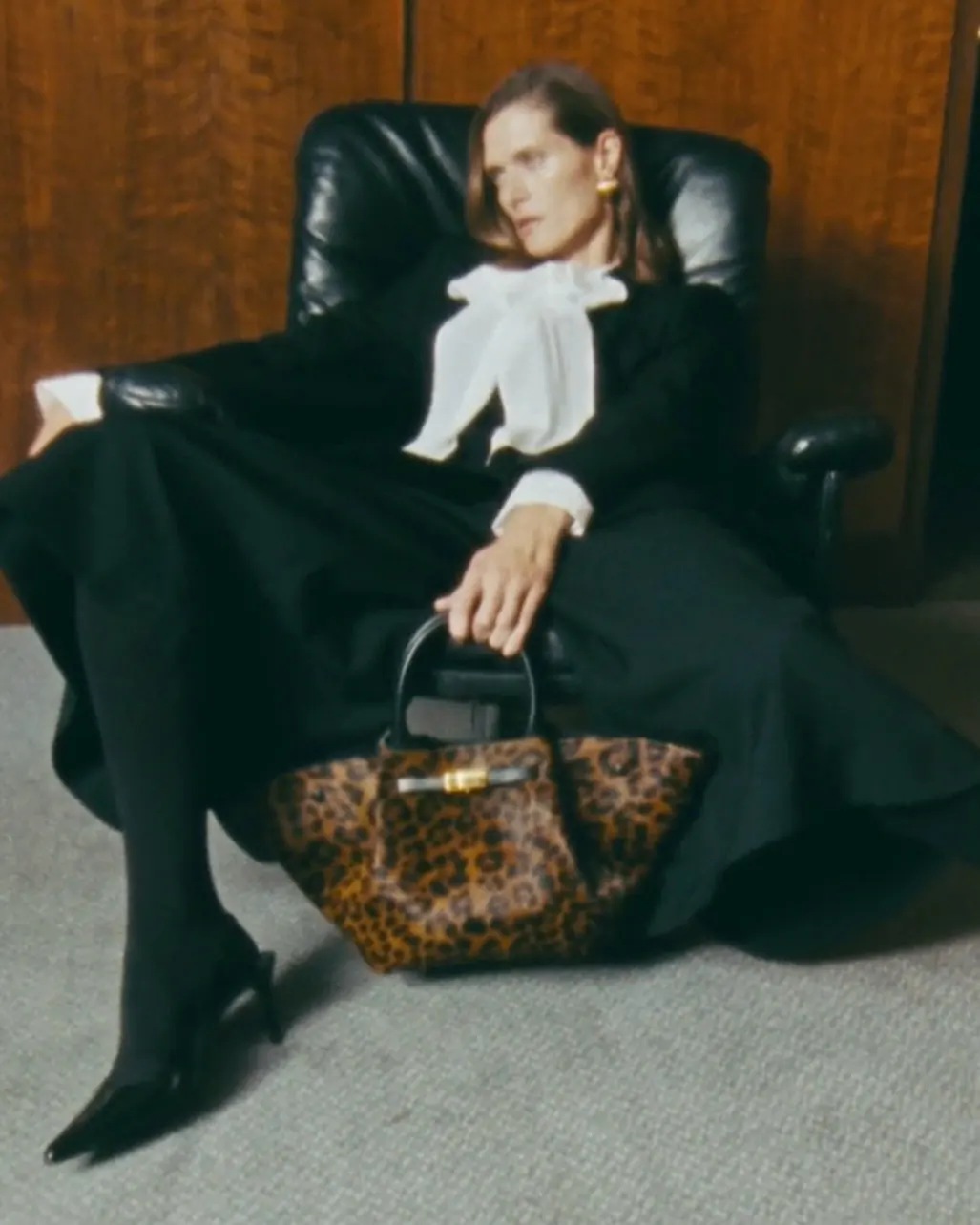 Woman seated in a dark chair holding a patterned handbag